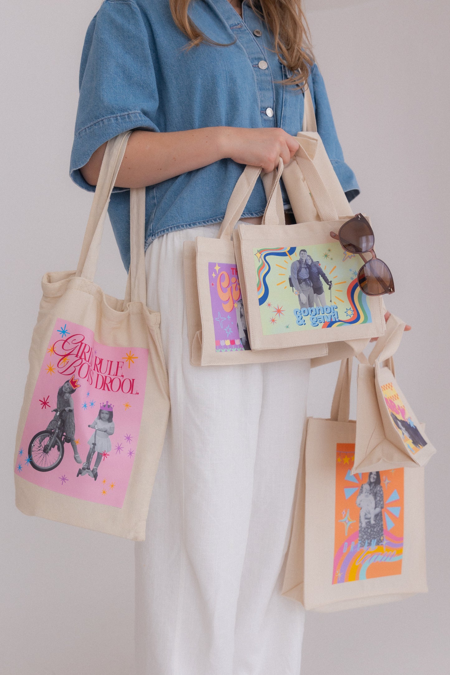 Person holding multiple tote bags with colorful designs against a plain background