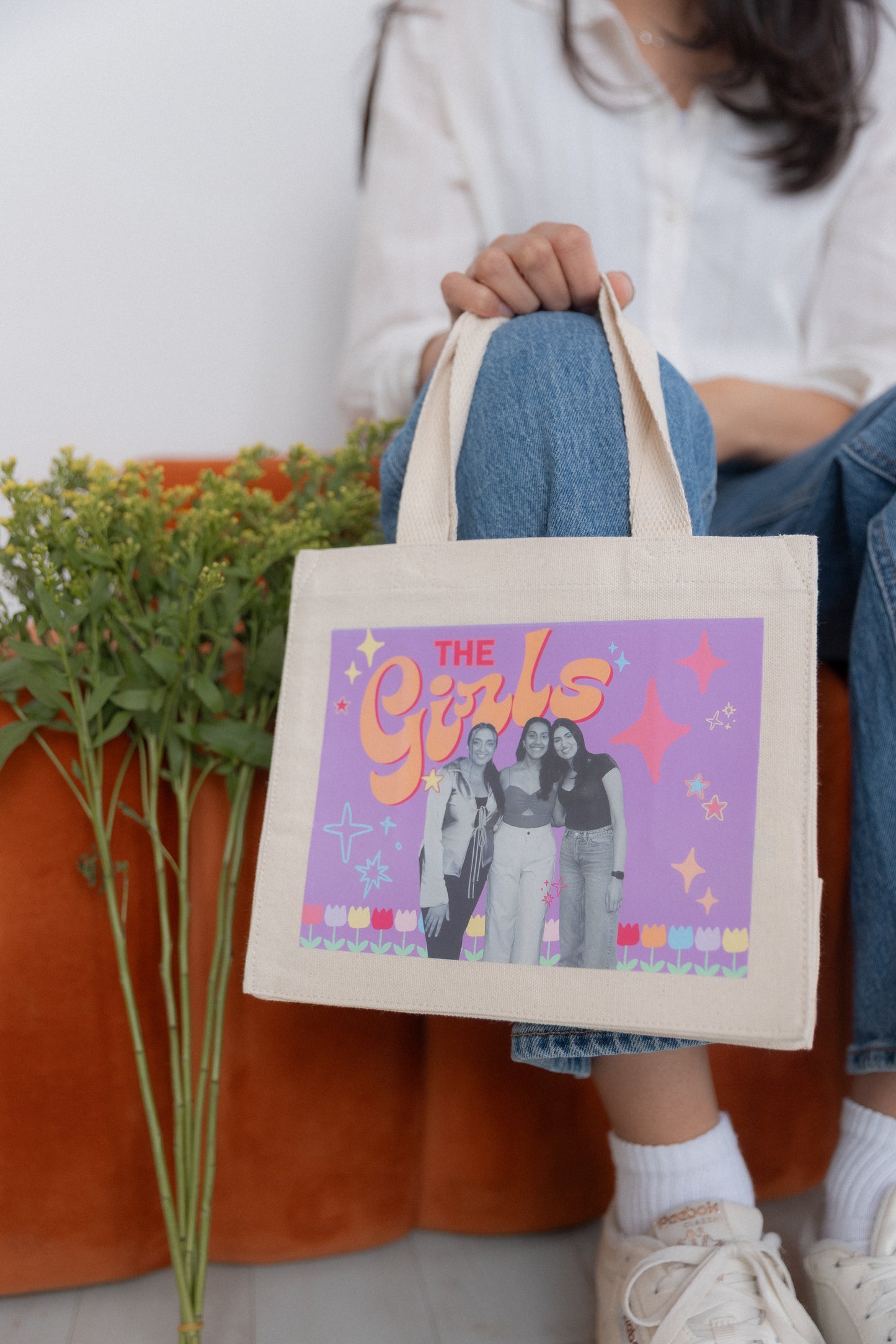 Person holding a tote bag with 'The Girls' graphic design.