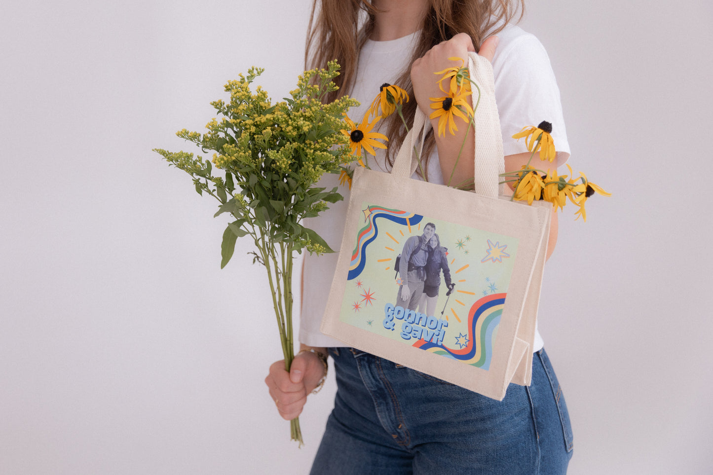 Person holding a tote bag with a design and flowers against a plain background