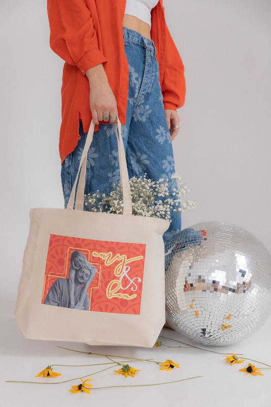 Person holding a tote bag with a design and a disco ball on a light background