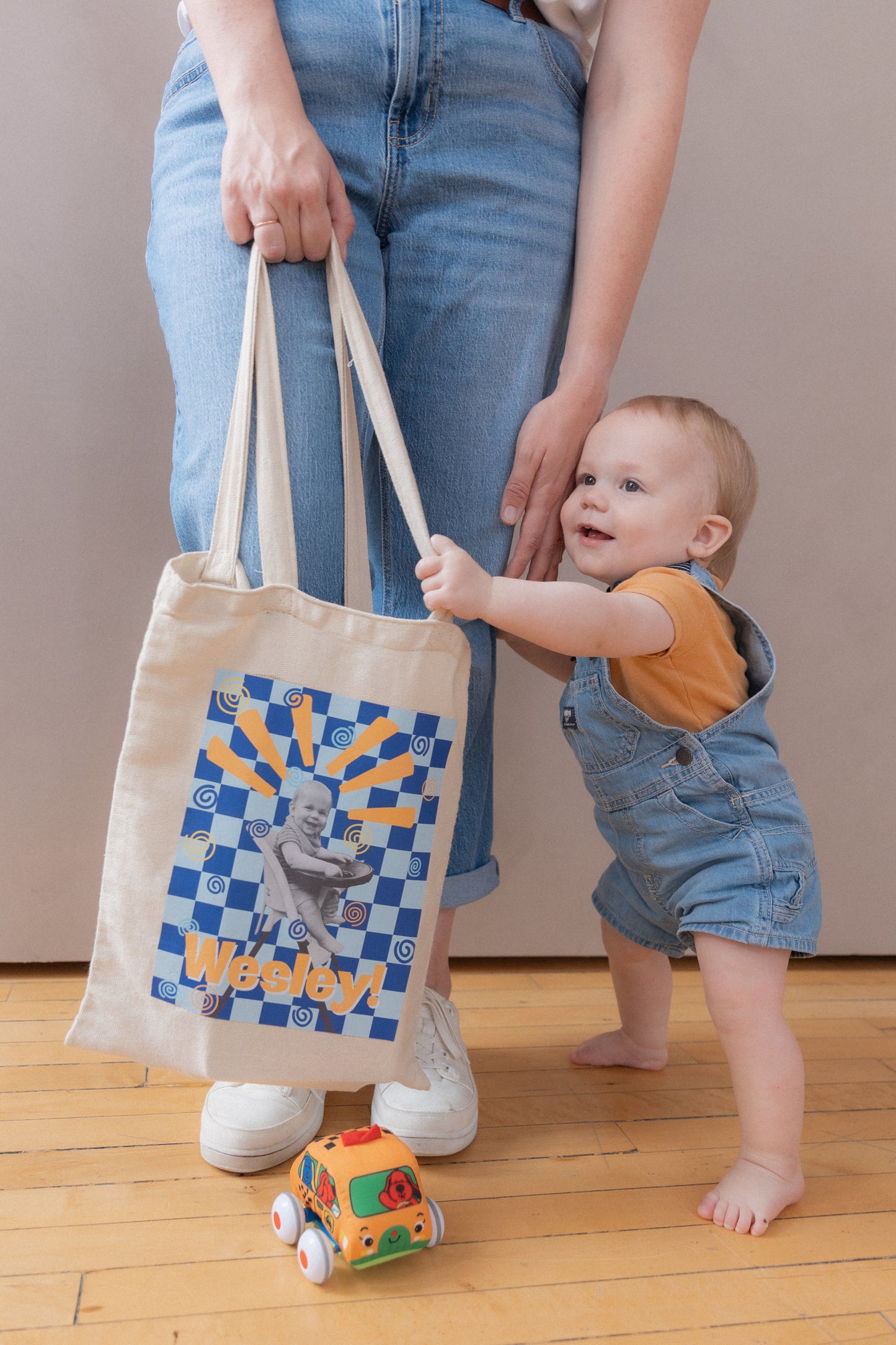 Person holding a tote bag with a child standing next to them on a wooden floor.