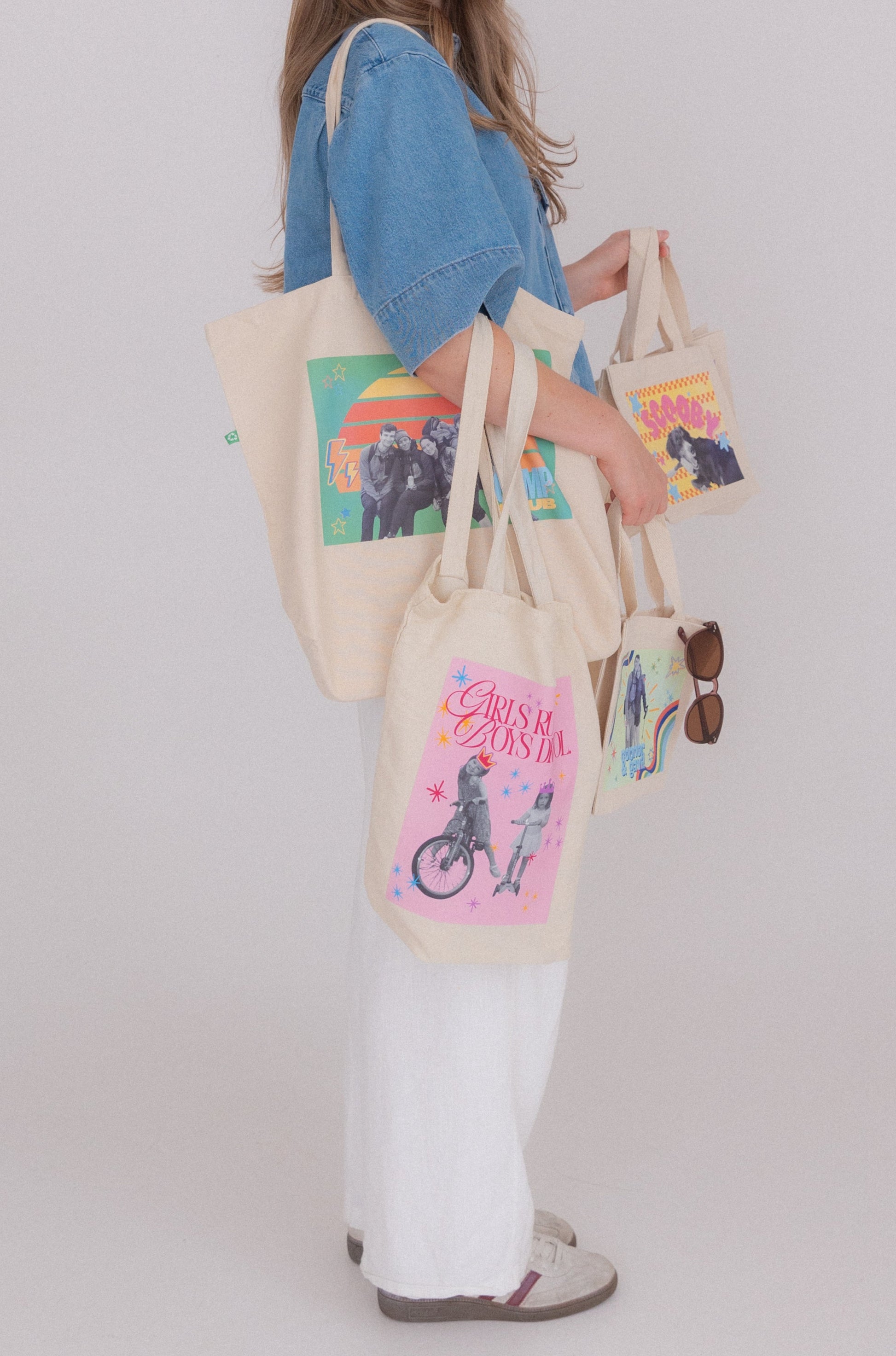 Woman holding multiple tote bags with colorful designs on a plain background
