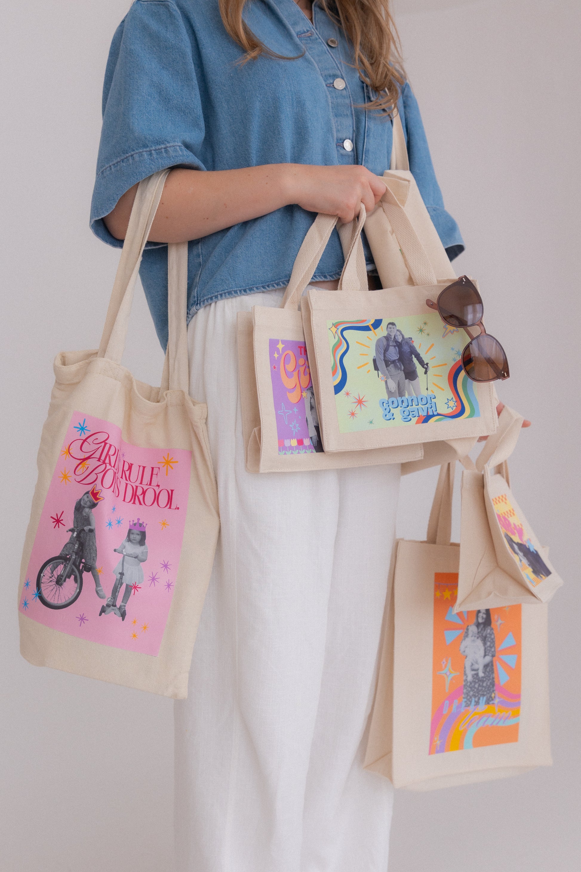 Person holding multiple tote bags with colorful designs against a plain background